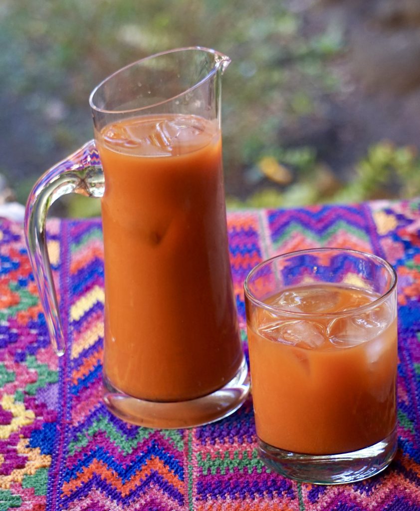 Pitcher and glass of fresco de tiste over ice on a colorful Guatemalan textile with a soft blurred background