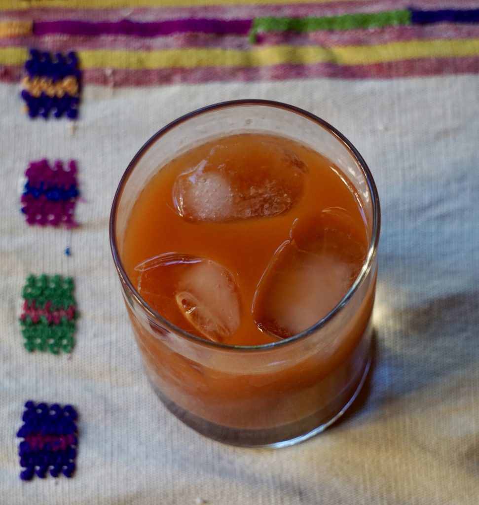 Vista superior de un vaso de fresco de tiste con hielo sobre tela guatemalteca blanca bordada con cuadros de colores