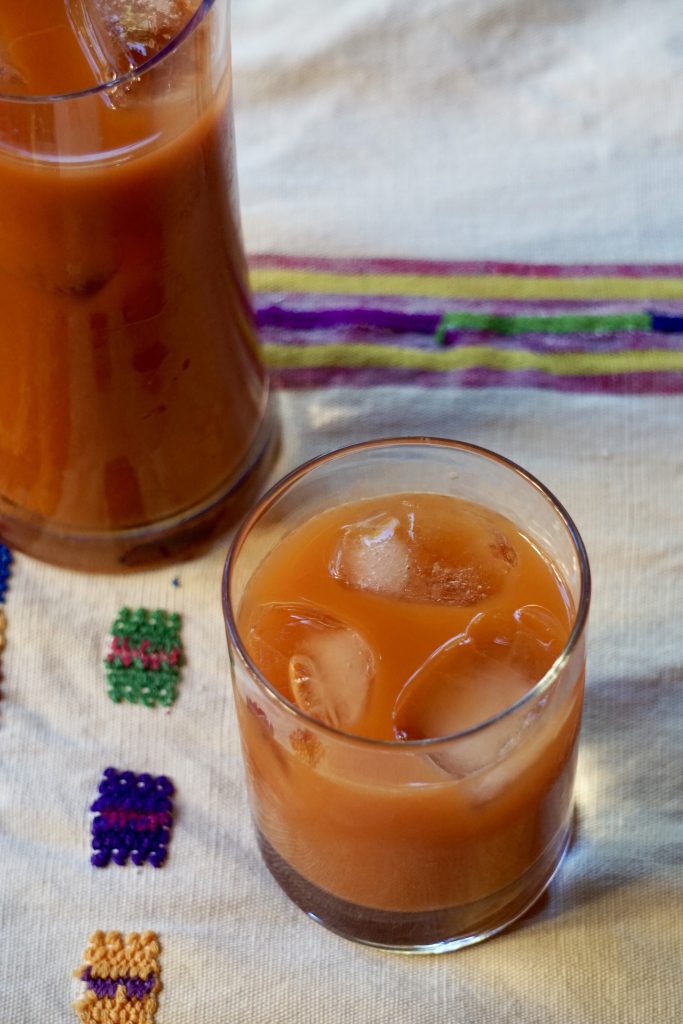 Glass and pitcher of fresco de tiste over ice on a white Guatemalan embroidered cloth with colorful stitched squares in soft natural light