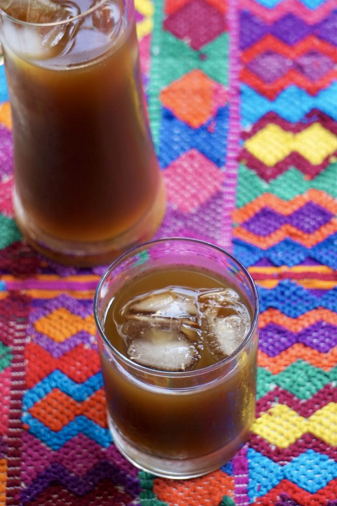 Pichel y vaso de fresco de chilacayote con hielo sobre un mantel bordado guatemalteco