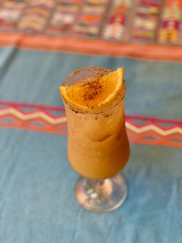 Top-down view of a fresco de pepita in a tall glass with a spiced pepita rim and cinnamon-dusted mango garnish on a blue Guatemalan textile