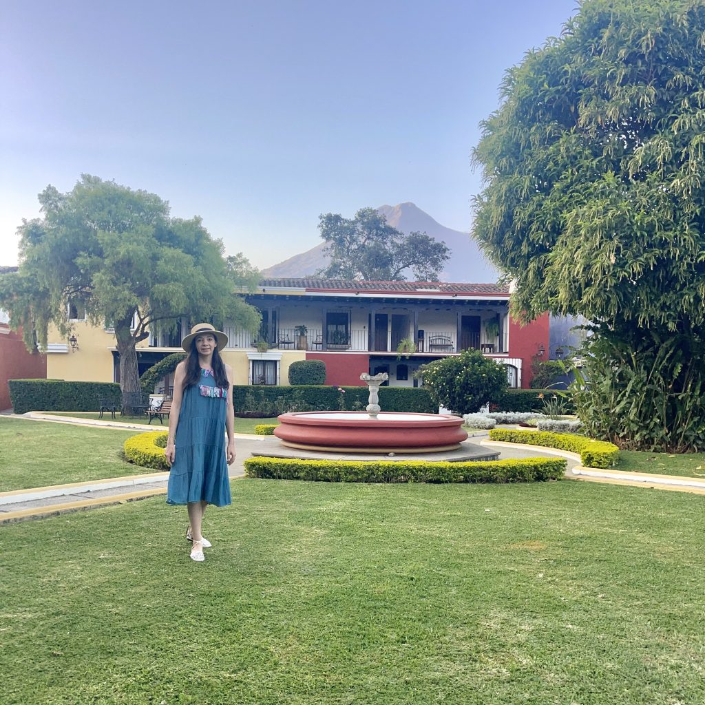 Jardín principal de Villa Colonial en Antigua Guatemala con fuente central, habitaciones con balcón y el Volcán de Agua al fondo