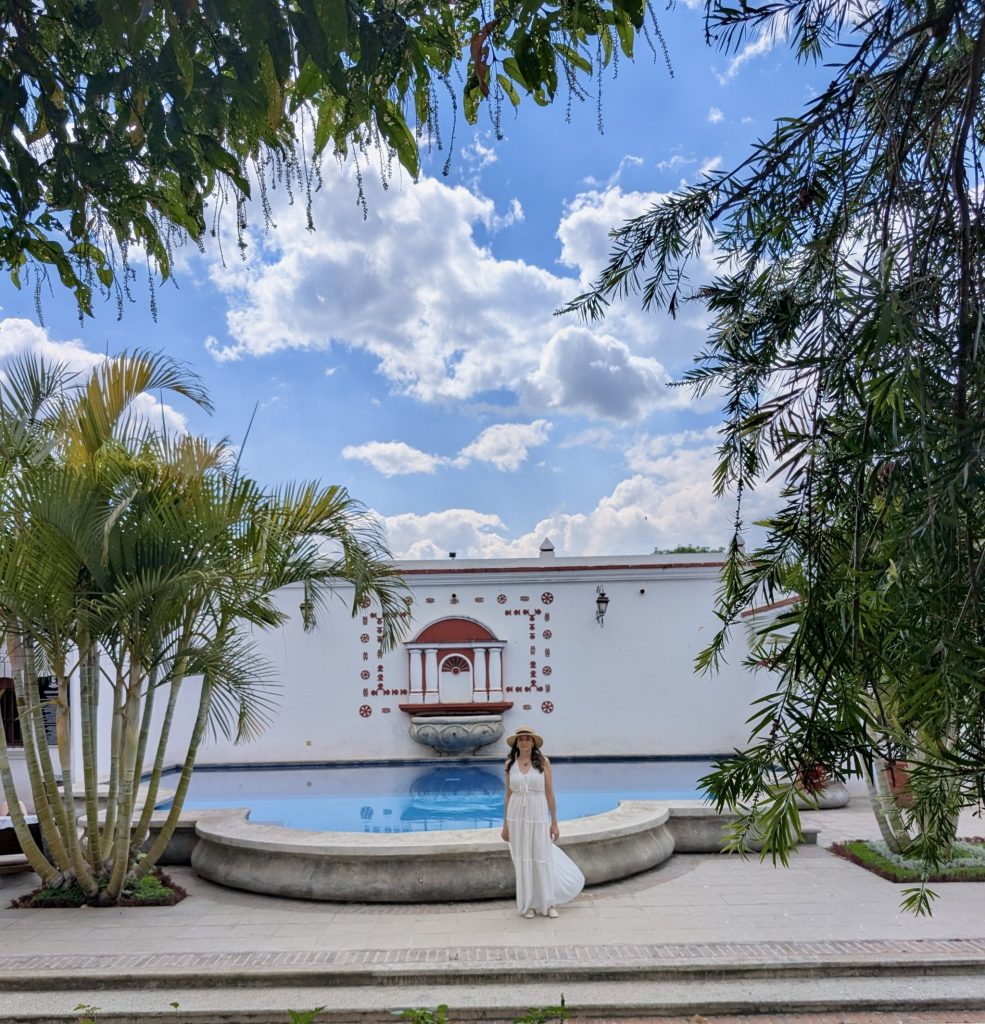 Vista panorámica de la piscina de Villa Colonial en Antigua Guatemala, rodeada de palmeras y enmarcada por la pared blanca con detalles coloniales en terracota