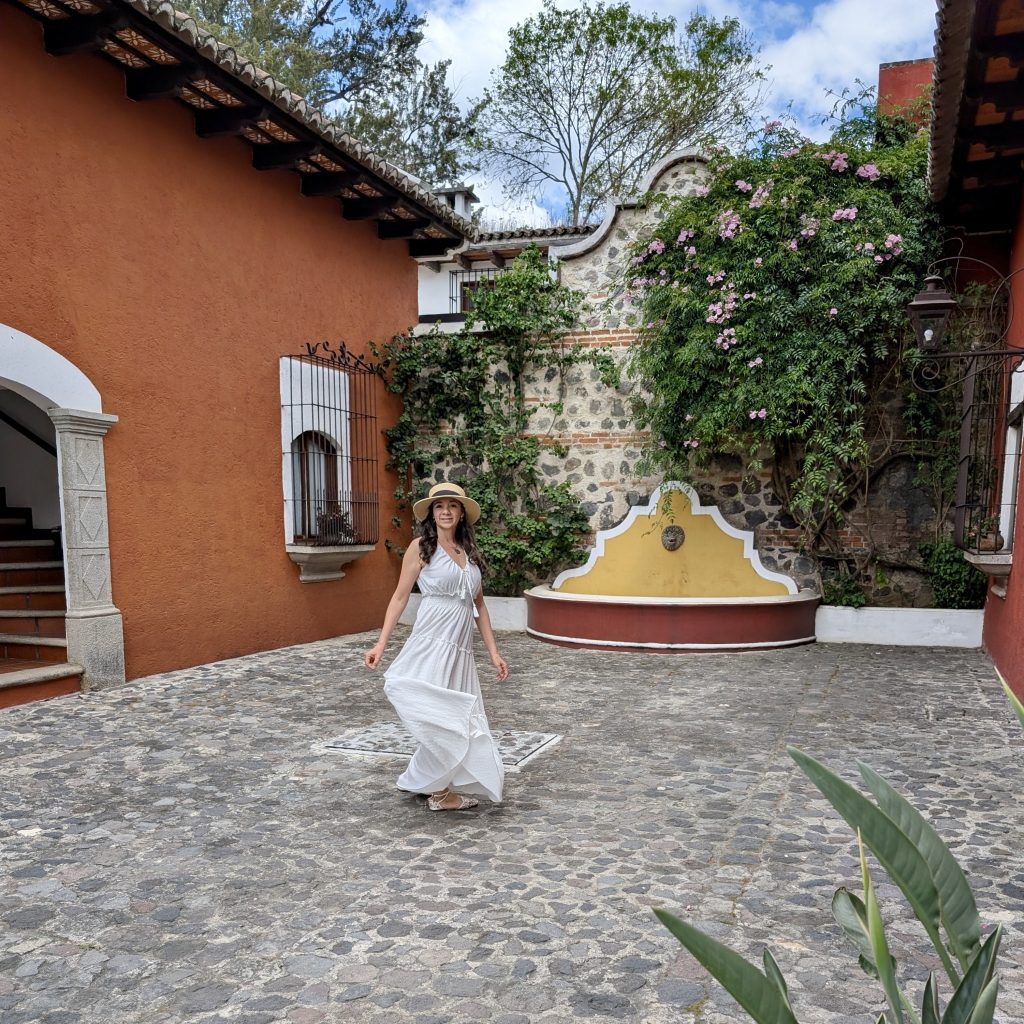 Inner cobblestone courtyard at Villa Colonial hotel in Antigua Guatemala with a yellow colonial fountain, bougainvillea-covered stone walls and terracotta building