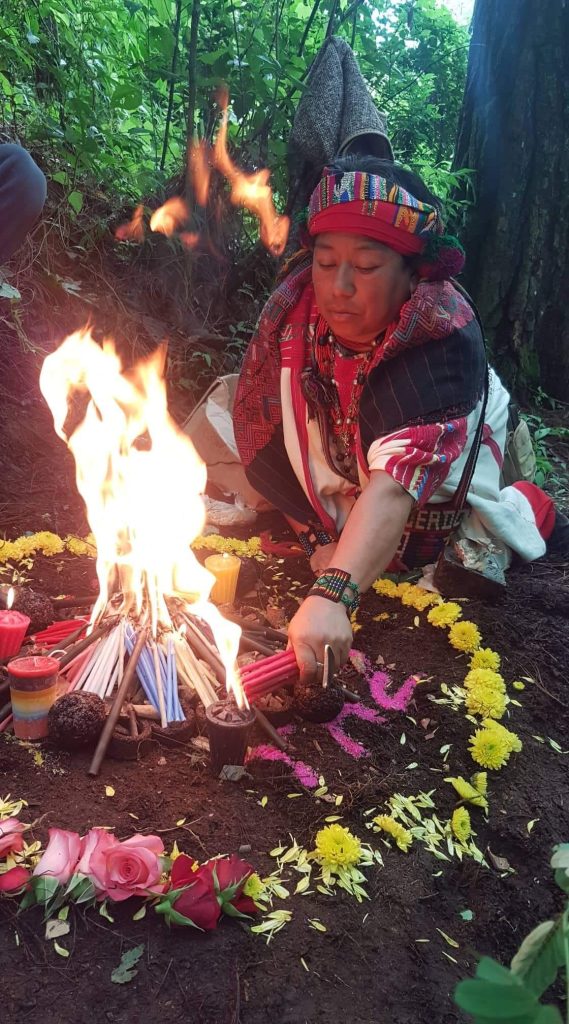 Mayan spiritual guide preparing a sacred fire ceremony surrounded by candles and flowers in Guatemala