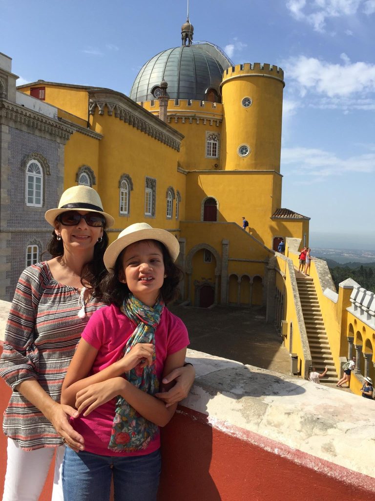 Mother and daughter in straw hats standing on the ramparts of the yellow Pena Palace Sintra Portugal UNESCO