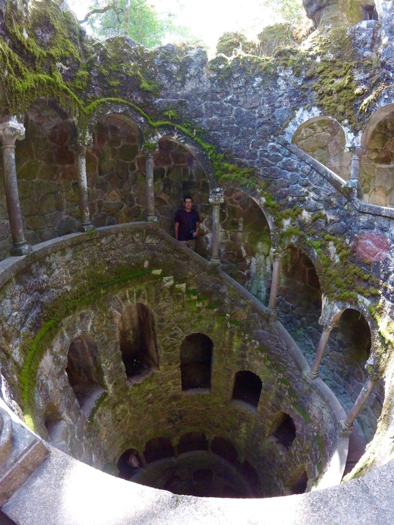 Man standing inside the moss-covered spiral Initiation Well at Quinta da Regaleira Sintra Portugal