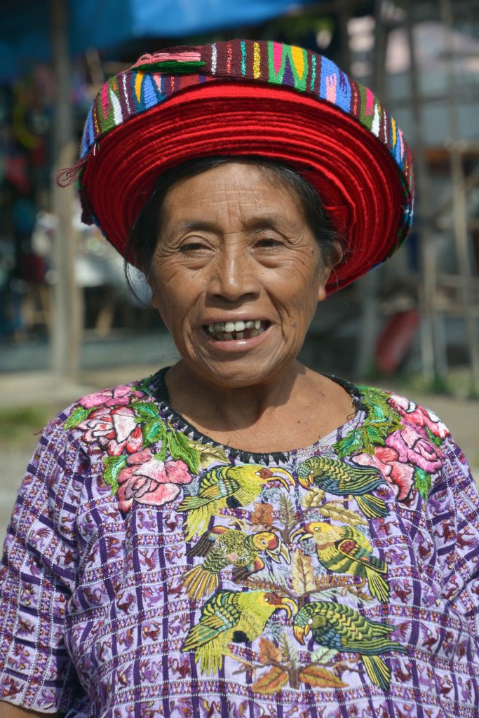 Smiling Tz'utujil Maya woman wearing a traditional embroidered huipil and red tocoyal headdress