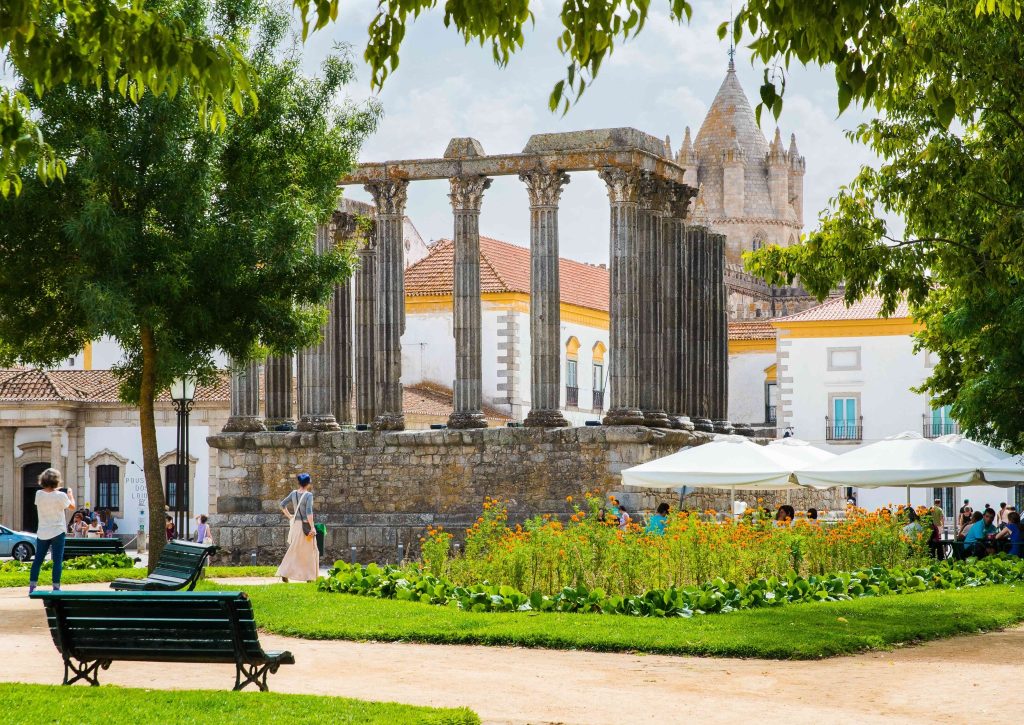 Roman Temple of Évora with Corinthian columns and Évora Cathedral behind it surrounded by green park and orange flowers Portugal UNESCO