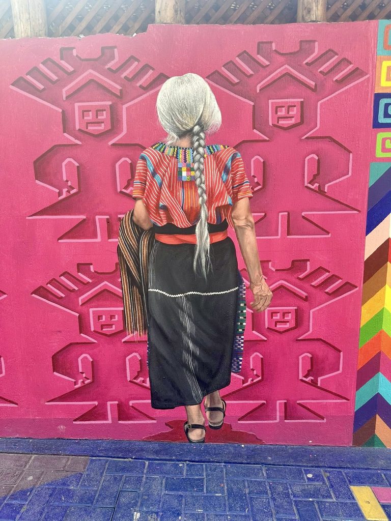 Elderly Indigenous woman standing in front of colorful mural in San Juan La Laguna Guatemala
