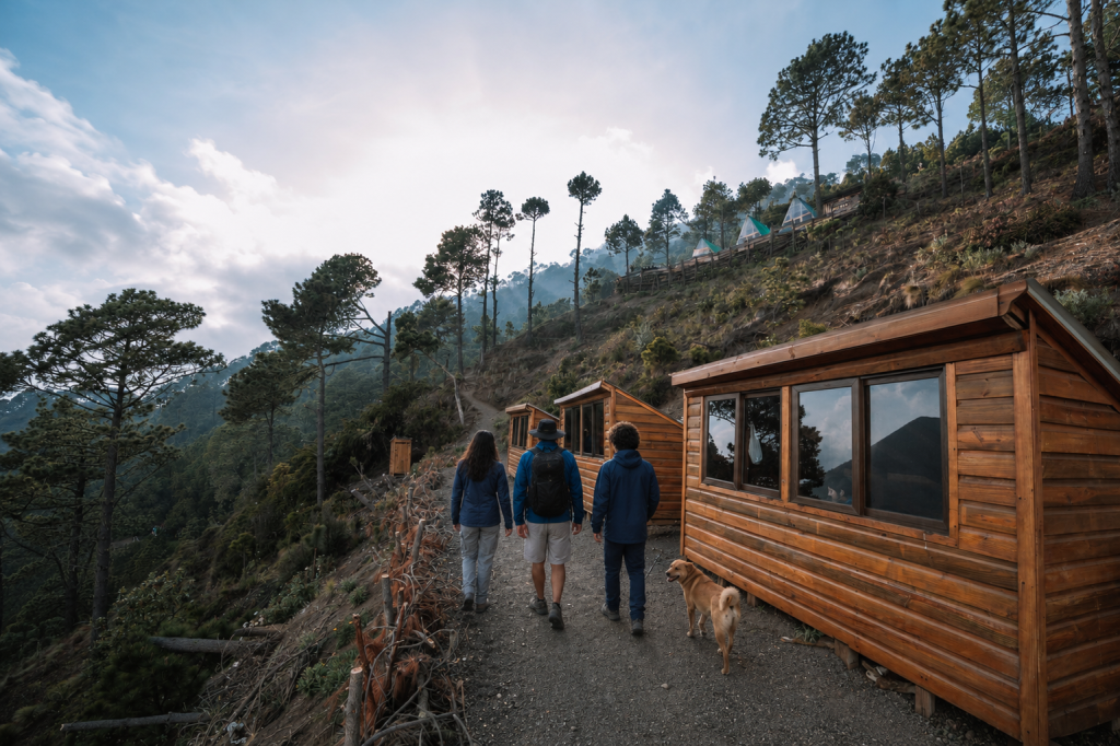 Wooden cabins at Acatenango volcano base camp with hikers walking past
