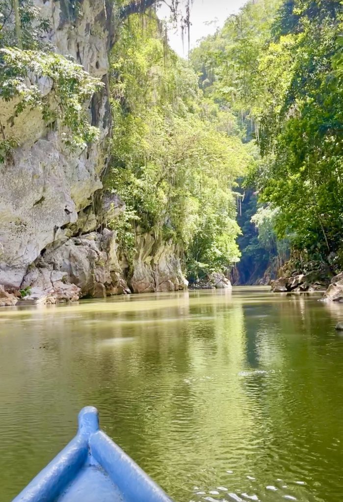 Cayuco boat entering El Boquerón Guatemala canyon with limestone cliffs, green river water, and jungle.