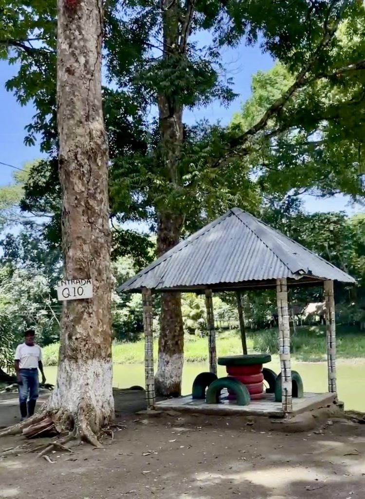 Entrance area at El Boquerón Guatemala with Q10 sign, trees, small shelter, and river nearby.