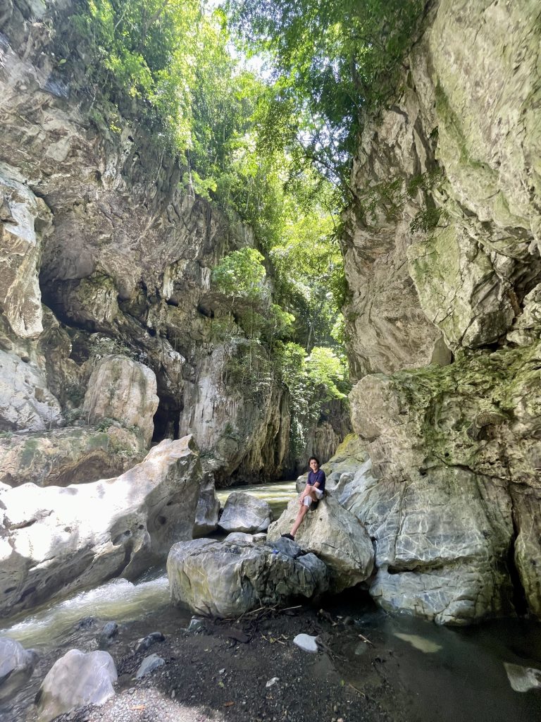 Traveler sitting on rocks inside El Boquerón Guatemala canyon surrounded by limestone cliffs and jungle.