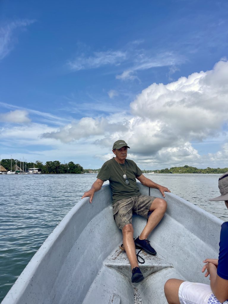 Man sitting at the front of a small boat on Río Dulce in Guatemala under a blue sky.