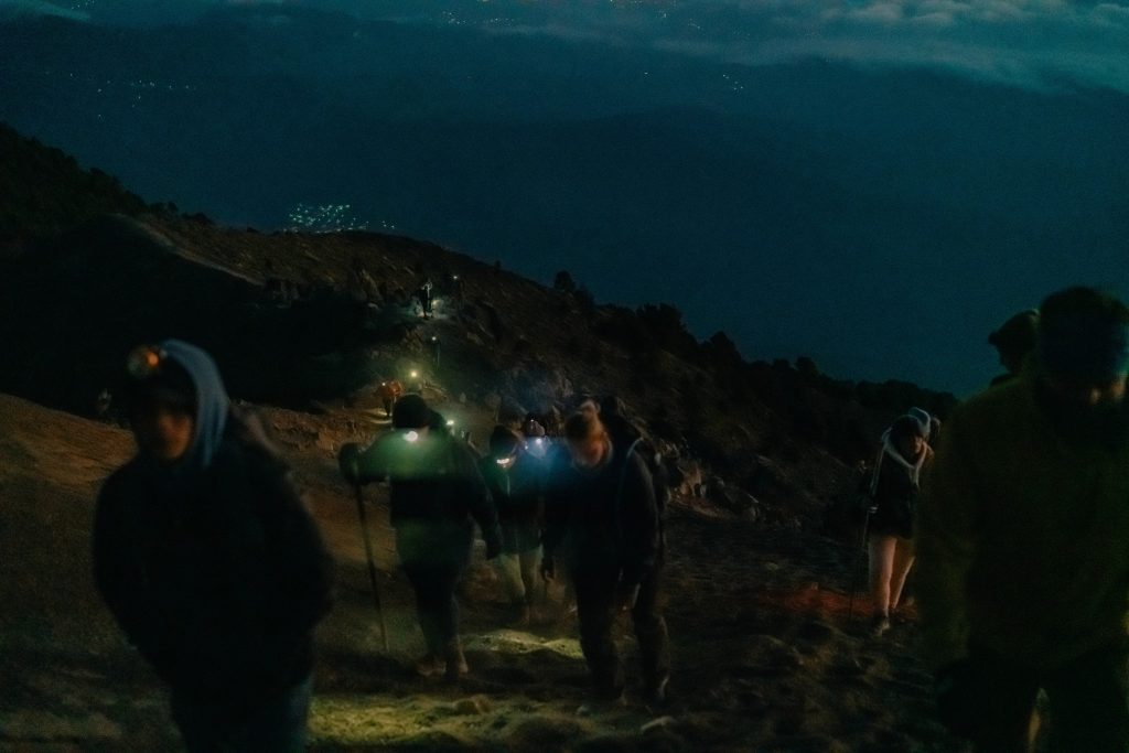 Hikers with headlamps walking toward Fuego volcano at night from Acatenango base camp