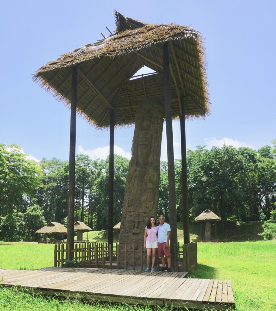Couple standing beneath the tallest Maya stela at the Quiriguá ruins, Guatemala