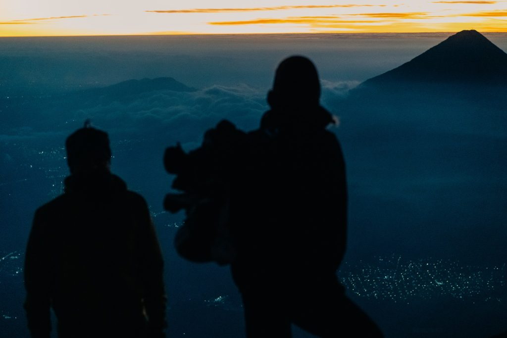 Silhouettes of hikers watching the sunrise from the Acatenango volcano summit