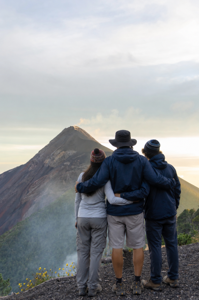 Three hikers standing together watching Fuego volcano erupt from Acatenango at dusk
