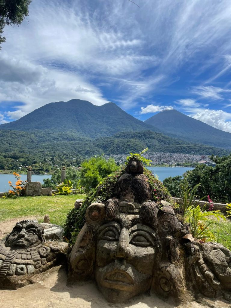 Carved stone faces at Chuitinamit, a Tz’utujil Maya archaeological site near Santiago Atitlán, with Lake Atitlán and volcanoes in the background.