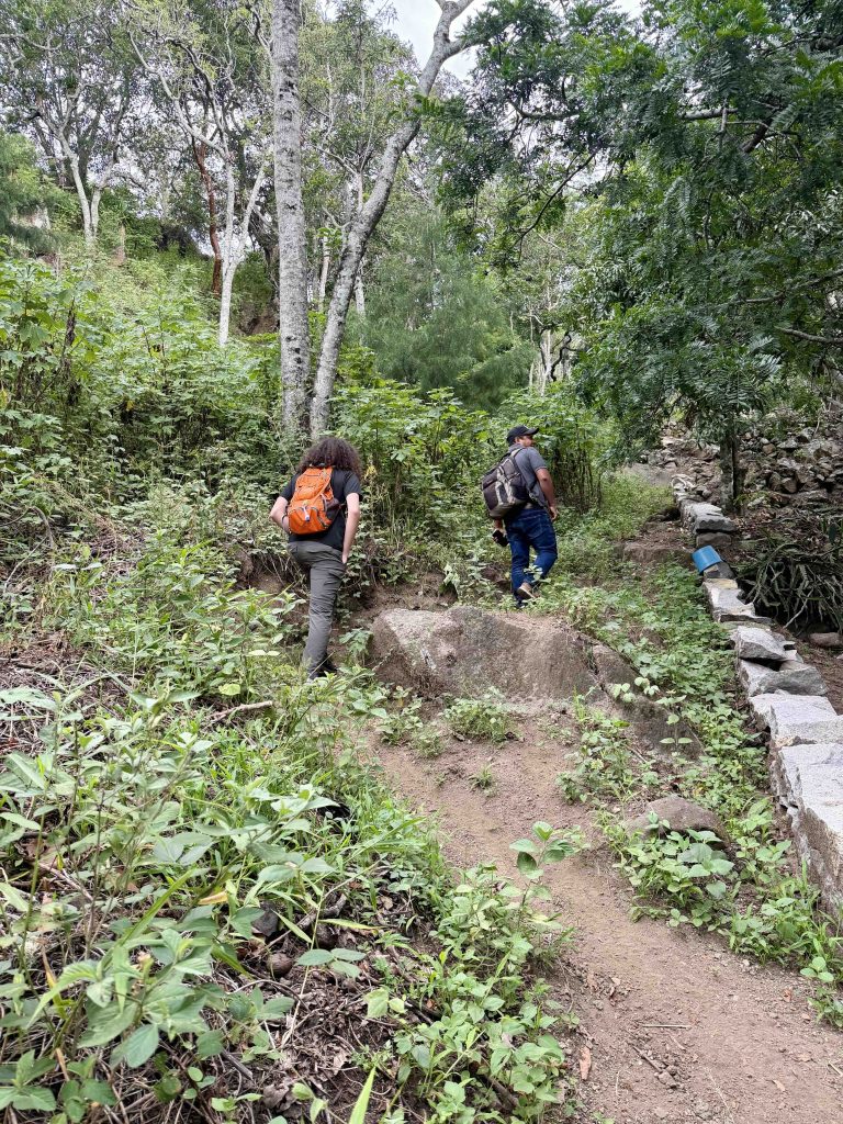 Hikers on the rustic uphill trail to Chuitinamit Santiago Atitlán, walking through private agricultural land.
