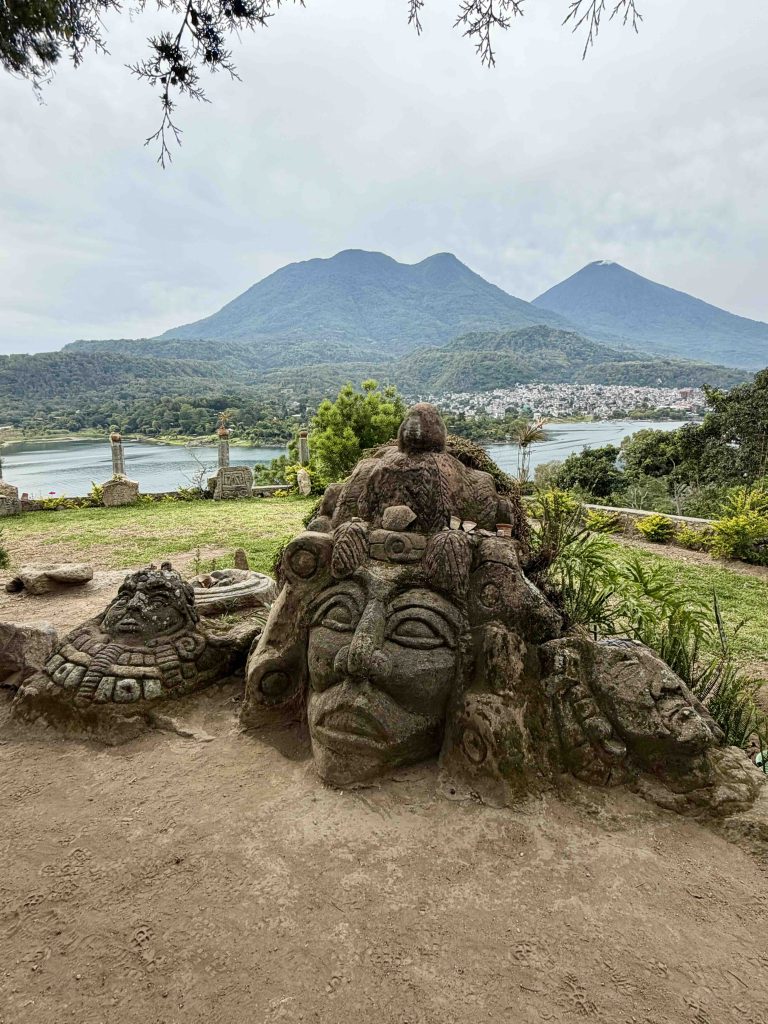 Carved stone figures at Chuitinamit near Santiago Atitlán with Lake Atitlán, Santiago and the volcanoes in the background.