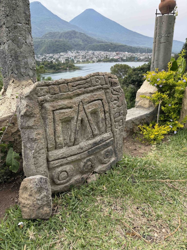 Chuitinamit Guatemala Maya archaeological site guide showing a carved stone overlooking Santiago Atitlán and the Lake Atitlán volcanoes