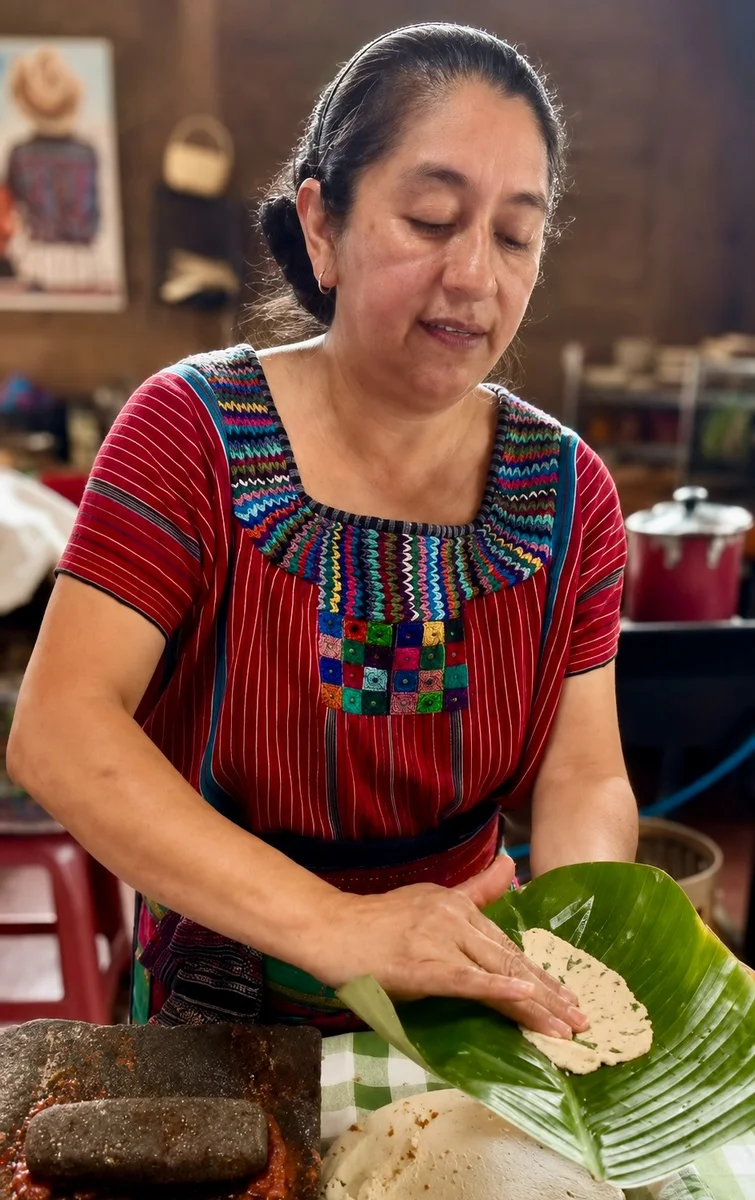 Cook in traditional Tz'utujil dress preparing masa on a banana leaf at Deleite Ancestral, San Juan La Laguna