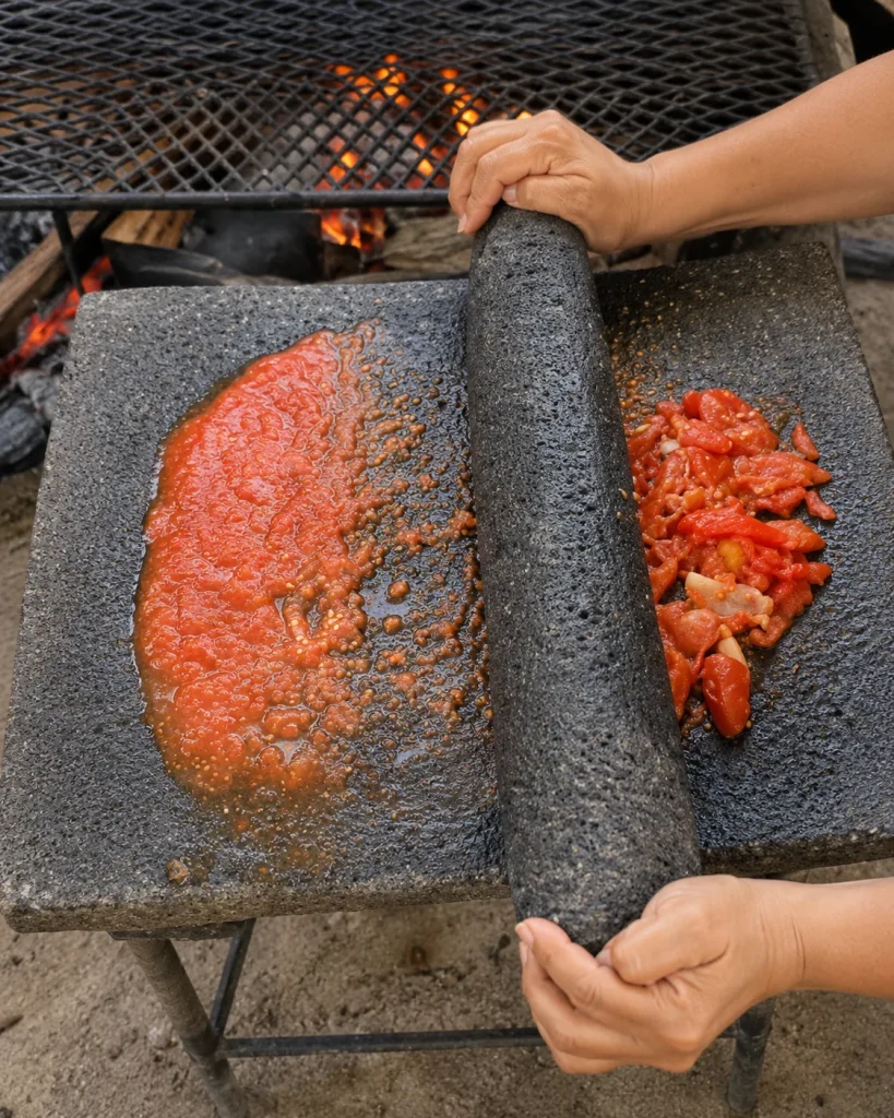 Tomato mixture being ground by hand on a traditional stone metate over a wood fire for a Guatemalan patín recipe