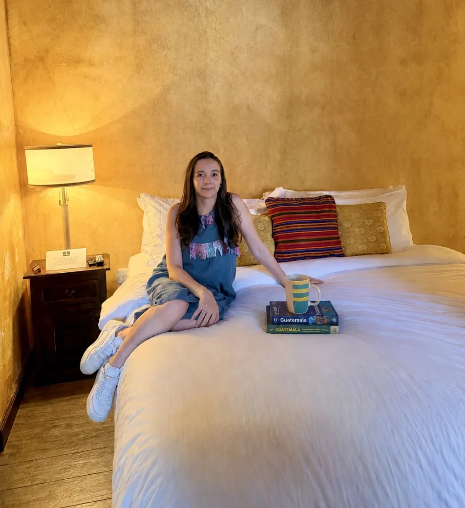 Guest sitting on a large bed inside a warm yellow suite at Hotel Casa Realeza in Antigua Guatemala.