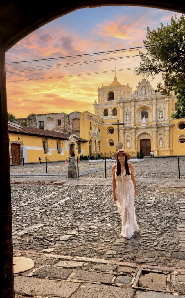 Guest walking beneath a colonial arch with La Merced Church and a colorful sunset in the background.