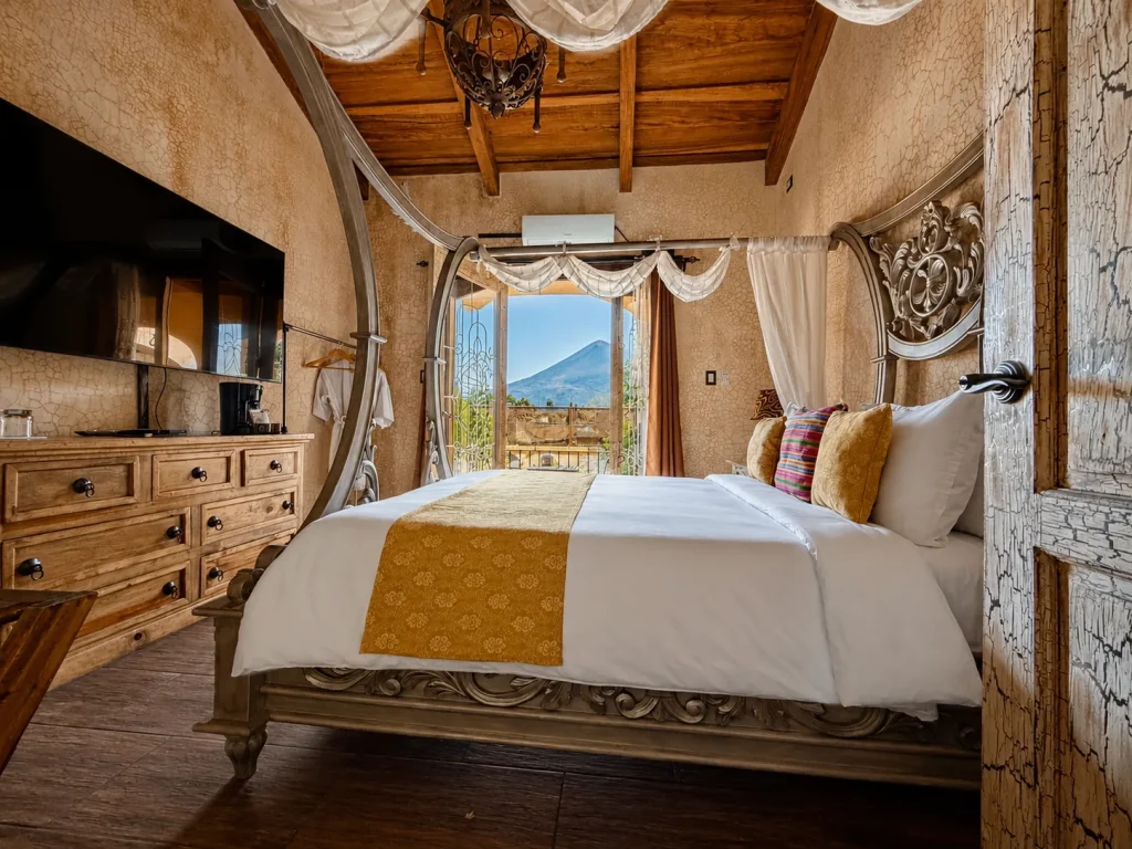 Ornate canopy bed inside a Casa Realeza suite with a volcano visible through the open balcony doors.